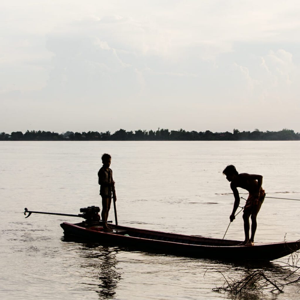 Young men puling in fish traps in the Mekong River, Cambodia.